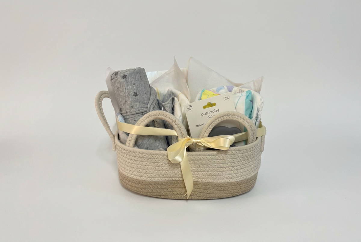 Starter Gift Basket with a grey blanket, Purebaby items and a cream ribbon bow, styled on a plain light grey studio background